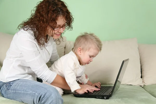 Молодая женщина в очках с ноутбуком и ребенком на диване — стоковое фото