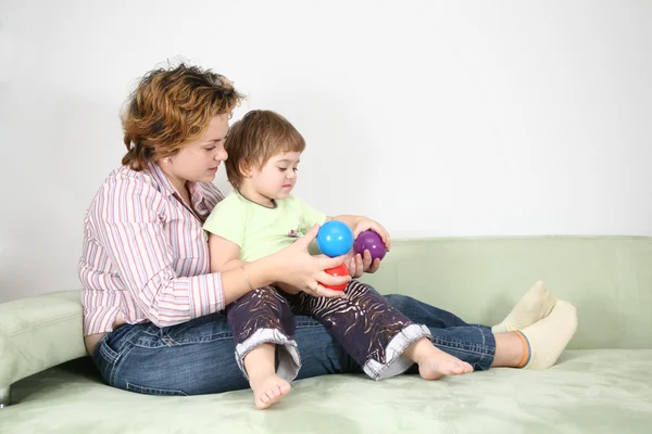 Matka s dítětem na pohovce, barevné koule — Stock fotografie