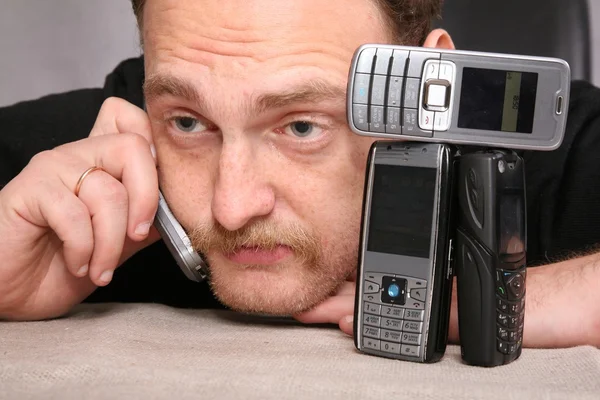Muž s plnovousem mluví na mobilu, spoléhat se na stůl — Stock fotografie
