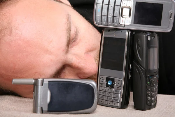 Человек с бородой будет спать на столе среди сотовых телефонов — стоковое фото