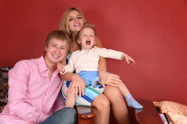 Jovem família rindo em poltrona na sala vermelha — Fotografia de Stock