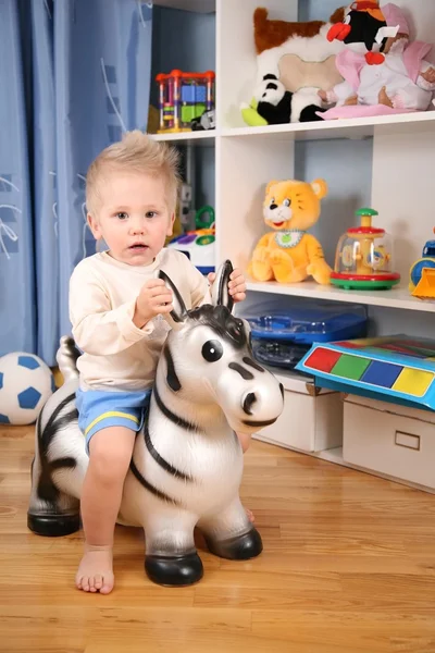 Маленький хлопчик в ігровій кімнаті на іграшковій зебри — стокове фото