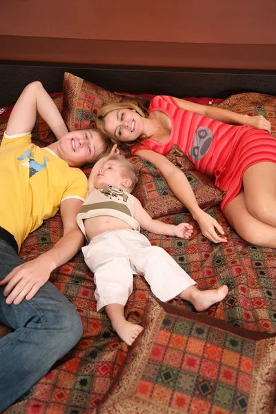 Family lies on red carpet on sofa — Stock Photo, Image