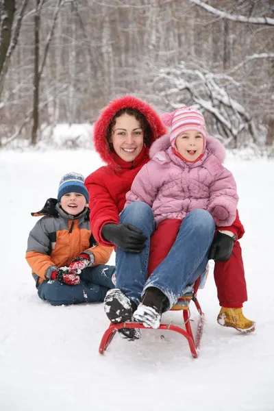 Mother sits on sled with children in park at winter — Stock Photo, Image