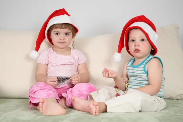 Deux enfants sur canapé en chapeaux santa claus — Photo