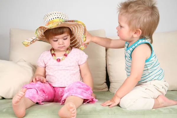 Boy and girl on sofa in straw hat with beads — Stock Photo, Image