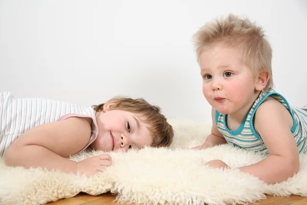 Two children lie on fur carpet — Stock Photo, Image