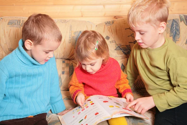 Дети читают книгу на диване в деревянной комнате — стоковое фото