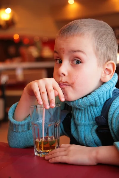 Chico sucio bebe jugo de vidrio a través de paja — Foto de Stock