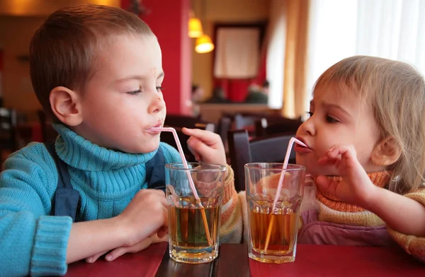 Little boy and girl drink juice from glasses through straws — Zdjęcie stockowe