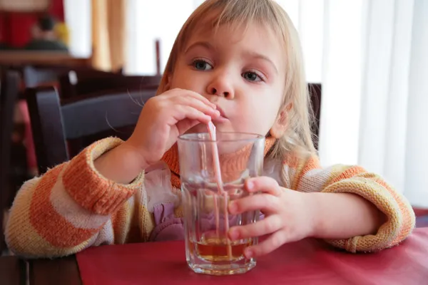 Маленькая девочка пьет сок из стекла через соломинку — стоковое фото