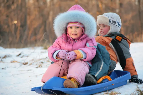 Children sits on plastic sled in park in winter — Stock Photo, Image