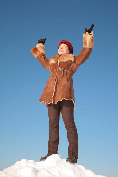 Симпатичная молодая женщина стоит на снежном холме с поднятыми руками — стоковое фото
