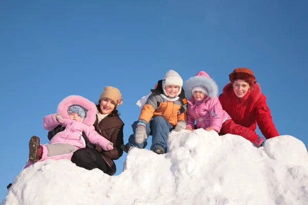 Duas mães com criança sentam-se na colina de neve — Fotografia de Stock
