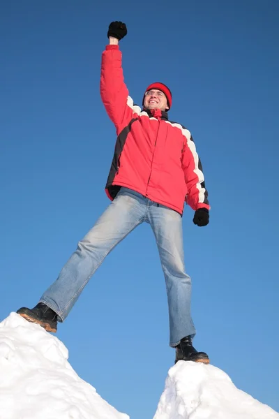 Muž v červené bundě na vrcholu kopce sněhu s rukou nahoru — Stock fotografie