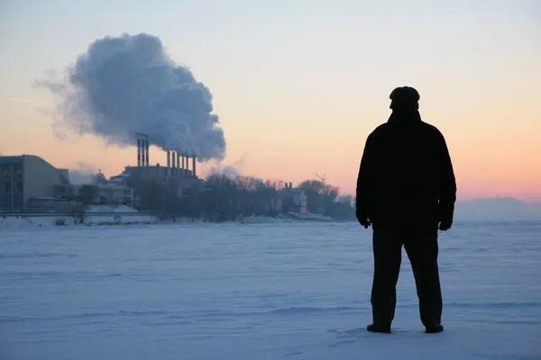 男子站在附近吸烟管道冰冻的河上 — 图库照片