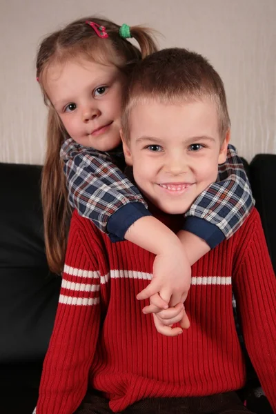 Girl embraces boy for the neck on sofa — Stock Photo, Image
