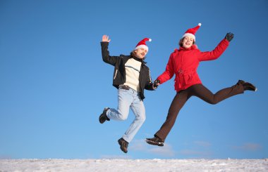 Couple jump on snow in santa claus hats clipart