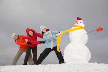 Three young girls pull snowman by yellow scarf clipart