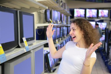Young woman in delight looks at TVs in shop clipart