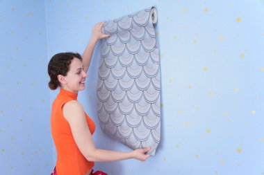 Young woman tries on wall-papers to wall clipart