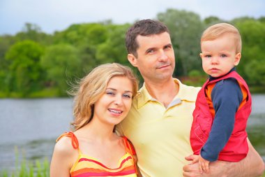 Father with child on hands and mother outdoors clipart