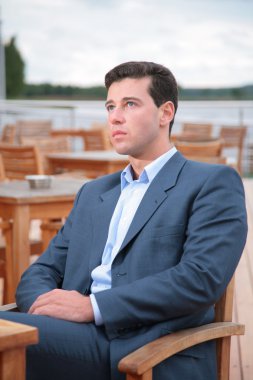 Portrait of man, who sits behind table in cafe near water clipart