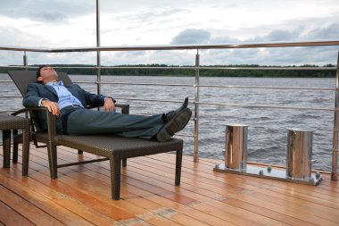 Portrait of man, who rests in chaise lounge on wharf near water clipart