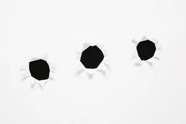 The sheet of paper with the three torn holes against the black background — Stock Photo, Image