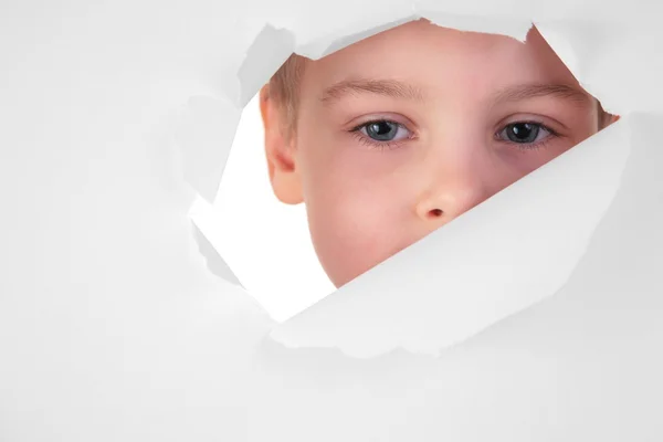 Мальчик смотрит в дыру в листе бумаги — стоковое фото