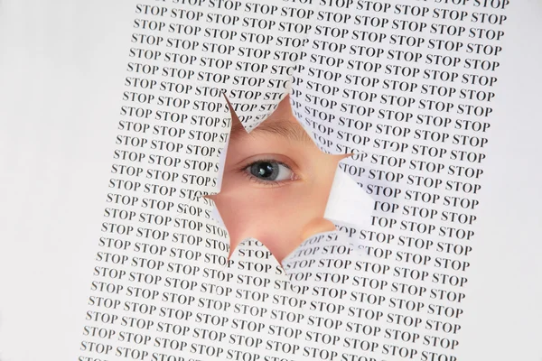 Eye looks into the hole in the sheet of paper with the printed word stop — Stock Photo, Image
