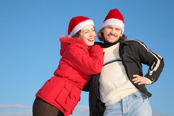 Couple against blue sky background in winter in santa claus hats — Stock Photo, Image