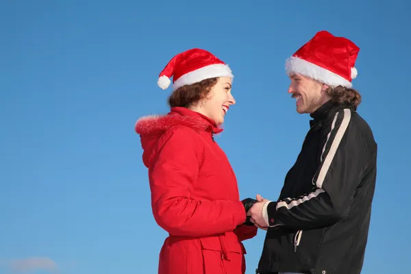 Pareja contra fondo azul cielo en invierno en Santa Claus sombreros de pie cara —  Fotos de Stock