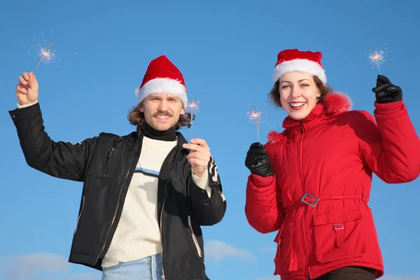 Couple against blue sky background in winter in santa claus hats with spark — Stock Photo, Image