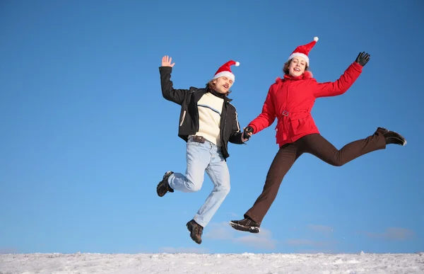 Casal saltar na neve em chapéus de santa claus — Fotografia de Stock