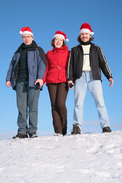 Three friends stand on snow in santa claus hats — Stock Photo, Image