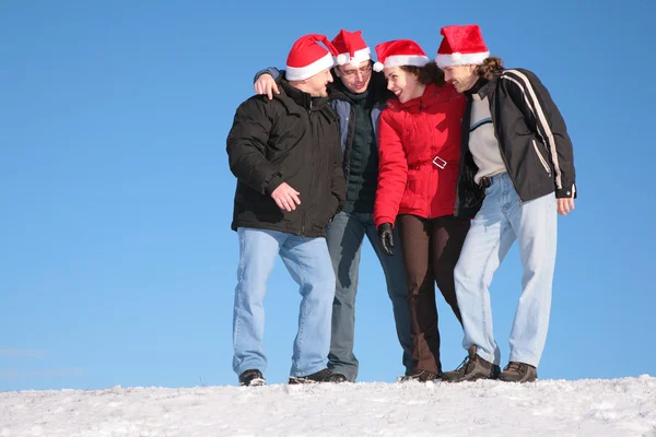 Quatro amigos falam sobre neve em chapéus de santa claus — Fotografia de Stock