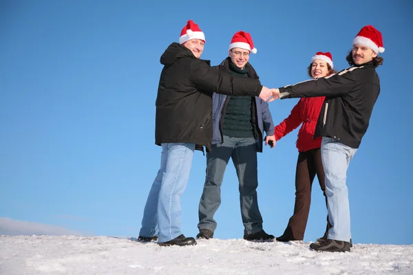 Four friends hold each other for hands on snow in santa claus hats — Stock Photo, Image