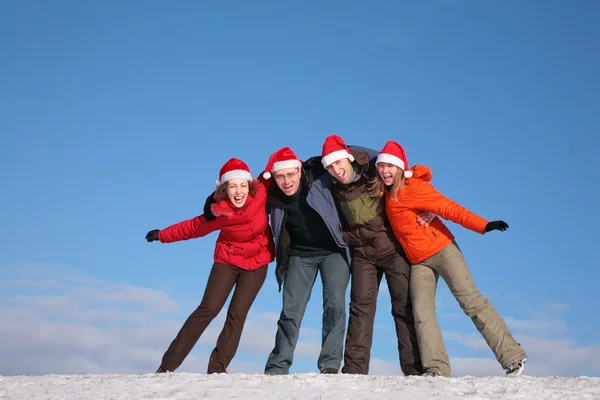 Cuatro amigos abrazándose en la cima de la colina de nieve en sombreros de Santa Claus —  Fotos de Stock