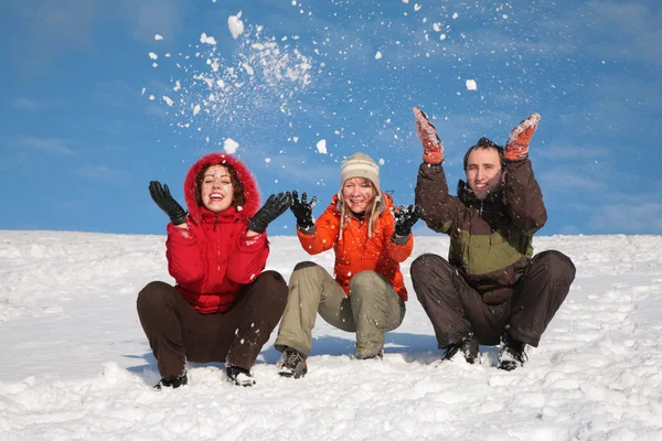 Tre vänner sitta på snö och kasta snön — Stockfoto