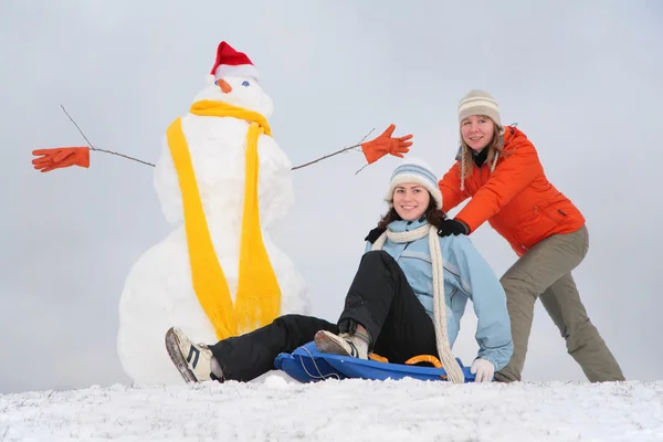 Δύο κορίτσια με πλαστικό έλκηθρο και χιονάνθρωπος — Φωτογραφία Αρχείου
