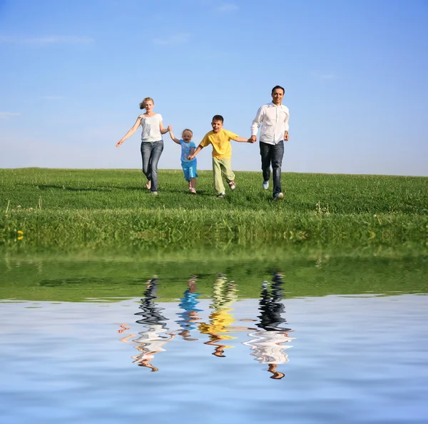 Family of four running grass sky water — Stock Photo, Image