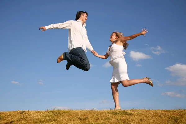 Man jumps on meadow hold girl from hand — Stock Photo, Image