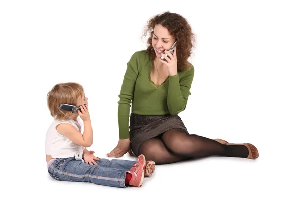 Mother and daughter sitting they talk on the cell phones on the the white — Stock Photo, Image