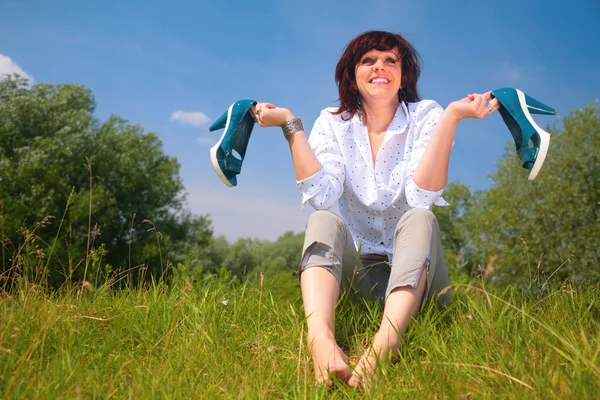 Kvinna sitter på gräset och rymmer skor i händer — Stockfoto