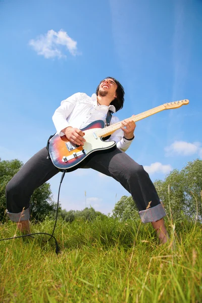 Mladý muž hraje na kytaru na trávě — Stock fotografie