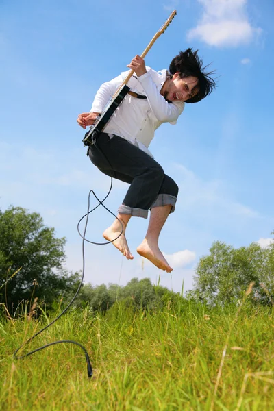 Mladý muž skočí s kytarou na trávě — Stock fotografie