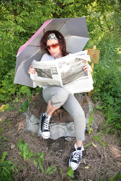 Frau sitzt auf gusseiserner Luke unter Regenschirm mit Zeitung — Stockfoto