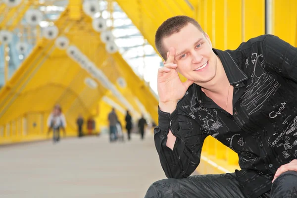 Sorridente ragazzo si siede sul ponte pedonale giallo — Foto Stock