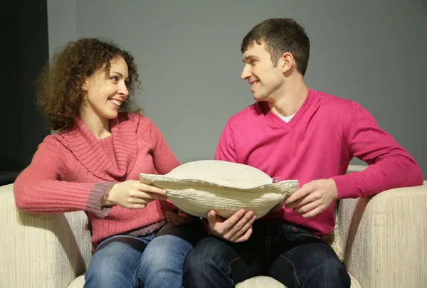 Couple sit on sofa with pillow and look at each other — Stock Photo, Image